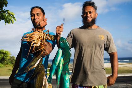 Two men hold freshly caught seafood in the Cook Islands.