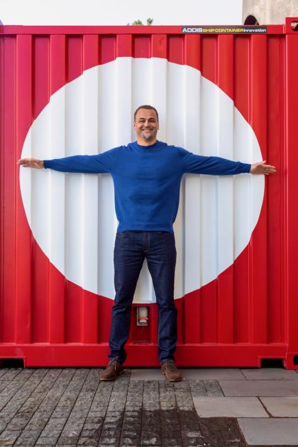 Scotty Morrison stands in front of a red shipping container, arms spread out