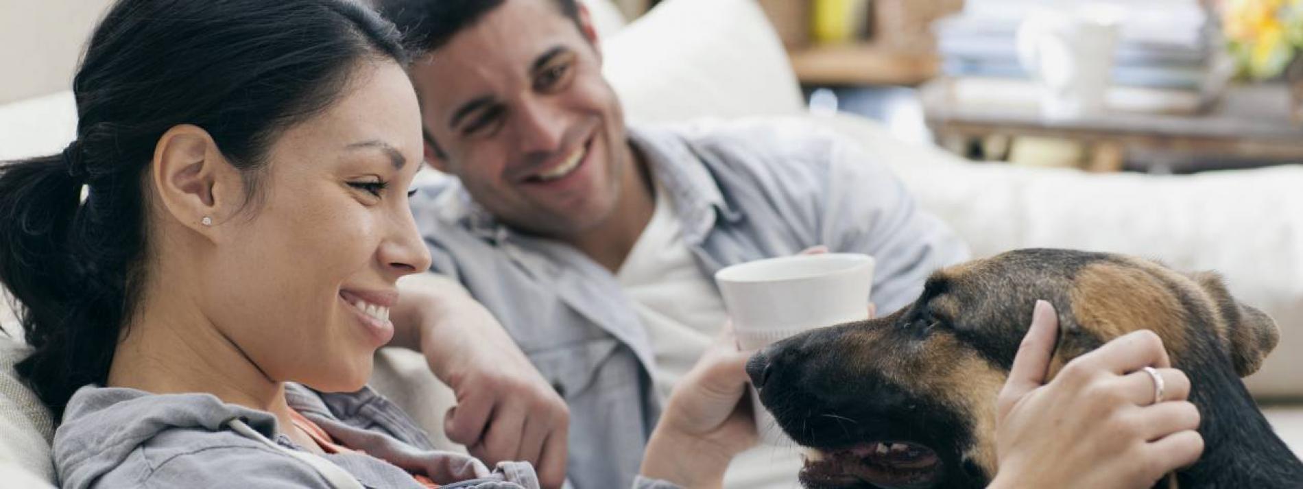 A woman and a man sitting on a couch with their dog