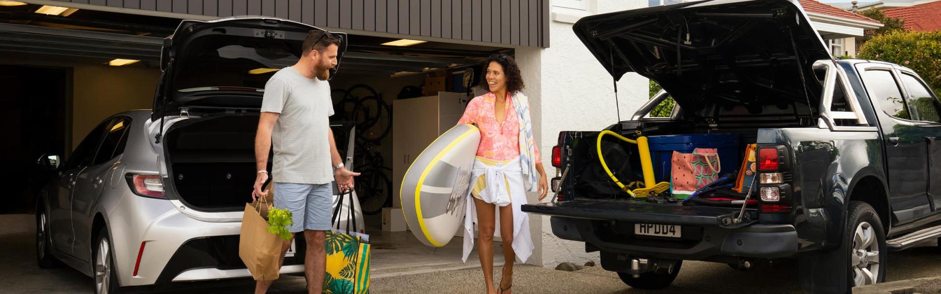 A couple organising paddleboard and beach supplies together outside garage